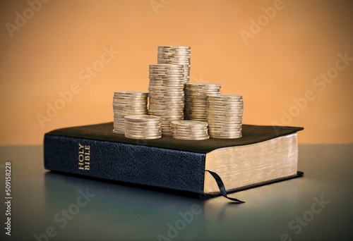 Fotografie A stack of coins with a Holy Bible Book in the background