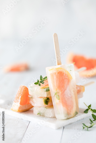 A grapefruit thyme popsicle leaning against a stack of the same popsicles.