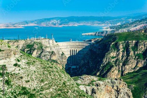 mountain landscape with an arched hydroelectric dam in the canyon and a reservoir in the valley photo