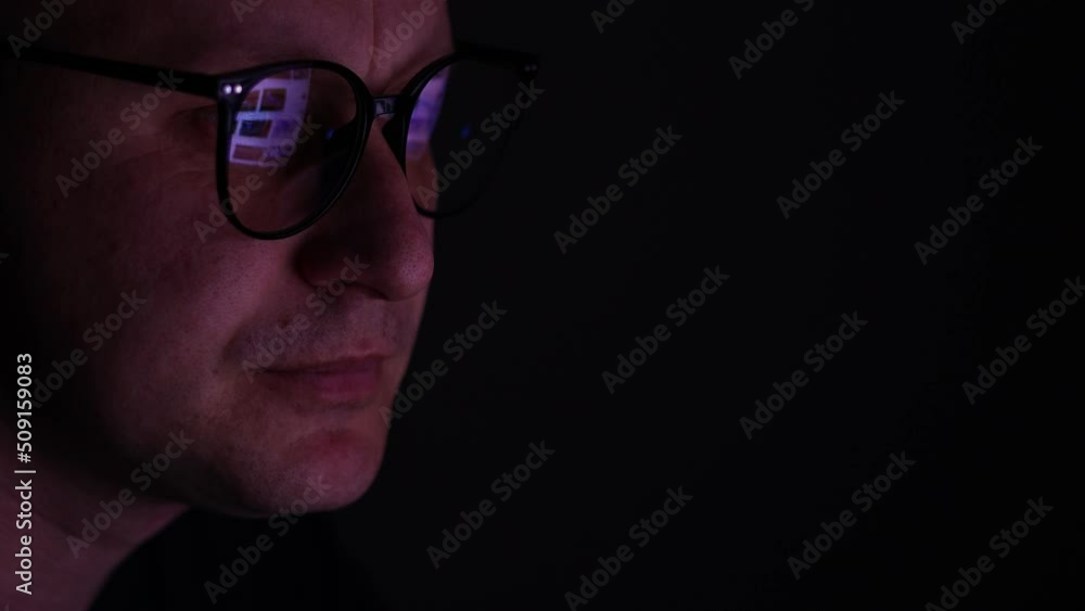 male working online late. Close up side view of focused man wears computer glasses for reducing eye strain blurred vision looking at pc screen with computer reflection using internet, watching. male working online late. Close up side view of focused man wears computer glasses for reducing eye strain blurred vision looking at pc screen with computer reflection using internet, watching.