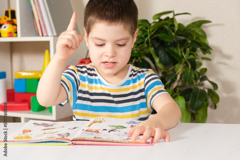 A happy boy of 4 years old looks at a book with pictures, shows pictures and names them. A happy boy of 4 years old looks at a book with pictures, shows pictures and names them.