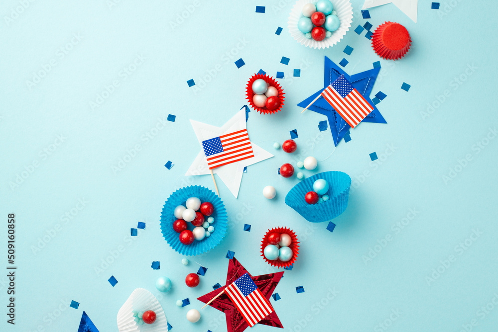 USA Independence Day concept. Top view photo of national flags stars confetti and paper backing molds with candies on isolated pastel blue background USA Independence Day concept. Top view photo of national flags stars confetti and paper backing molds with candies on isolated pastel blue background