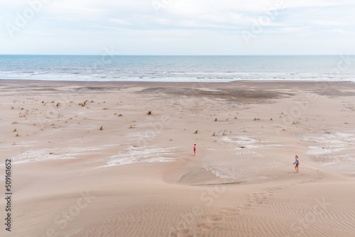 Aerial view of a mature mother and daughter from a big dune with the sea and the beach behind on a windy day. photo