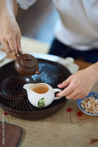 close up of hands pouring tea from teapot to teacup in a traditional asian tea chamber