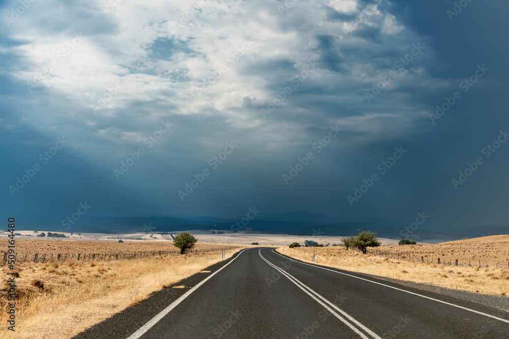 Straight open empty road surrounded by farms and fields just before the storm in Australia. Road trip travel