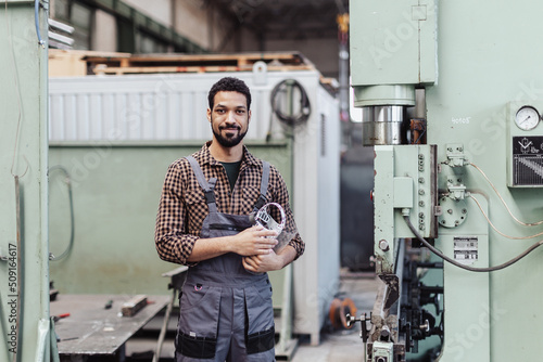 Portrait of engineer male welder standing near metal machine at industrial factory.
