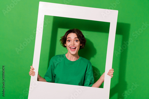 Photo of astonished positive lady hold paper album card look camera isolated on green color background photo