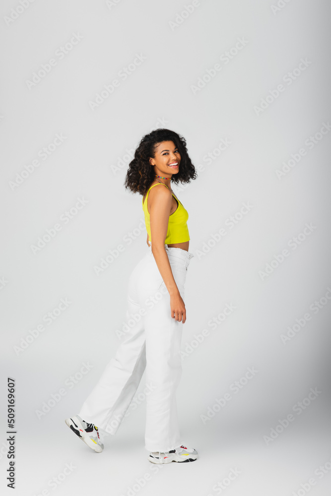 full length of happy african american woman in trendy outfit and stylish sneakers posing isolated on grey. full length of happy african american woman in trendy outfit and stylish sneakers posing isolated on grey.
