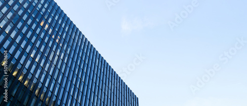 Modern high-rise building against the blue sky. Bottom view of a skyscraper in the business district. Low angle view of the glass facade of an office building. Banner with copy space.