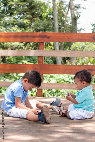 Vertical photo of two children playing. Little brothers playing in a wooden playpen outdoors.