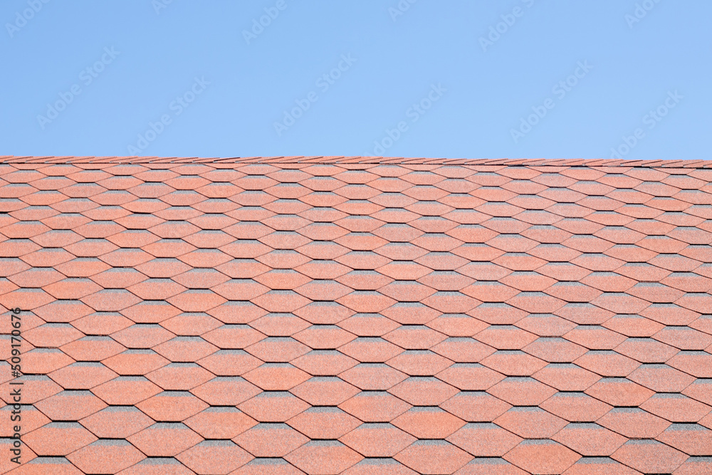New roof with red shingles against the blue sky. High quality photo. Tiles on the roof of the house. Use to advertise roof fabrication and maintenance. Spotted texture. Affordable roofing. New roof with red shingles against the blue sky. High quality photo. Tiles on the roof of the house. Use to advertise roof fabrication and maintenance. Spotted texture. Affordable roofing.