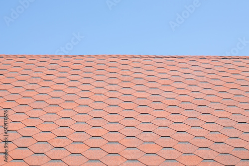 New roof with red shingles against the blue sky. High quality photo. Tiles on the roof of the house. Use to advertise roof fabrication and maintenance. Spotted texture. Affordable roofing.
