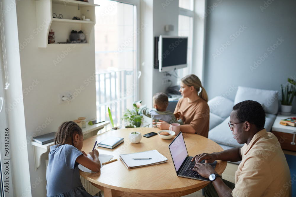 High angle portrait of black man using laptop at home with wife and children around him, copy space