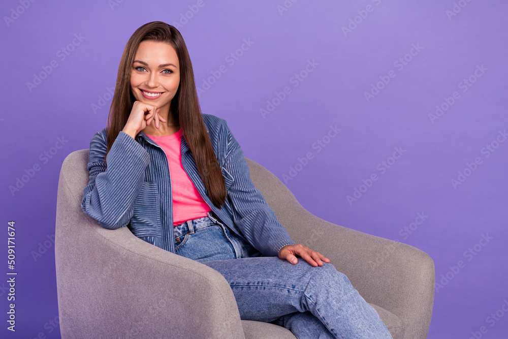 Photo of adorable satisfied lady sitting chair arm touch chin toothy smile isolated on violet color background Photo of adorable satisfied lady sitting chair arm touch chin toothy smile isolated on violet color background