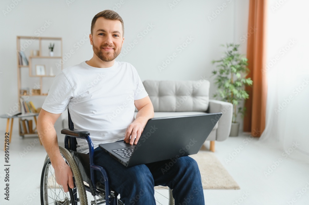 Man in wheelchair working on laptop in living room Man in wheelchair working on laptop in living room