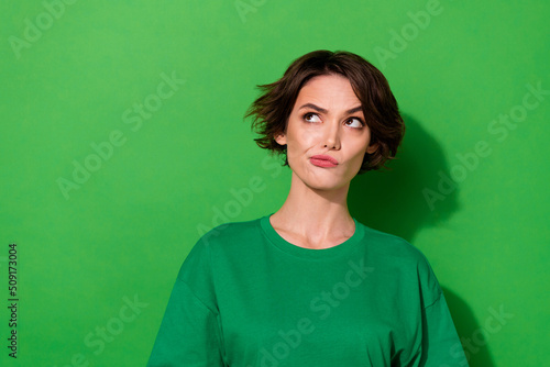 Photo of doubtful unsure young lady dressed casual t-shirt looking empty space isolated green color background
