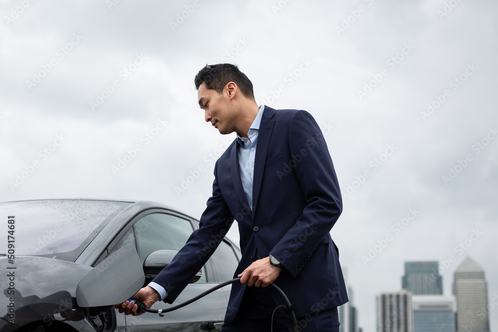 © ReeldealHD images - Businessman charging electric car in the city © ReeldealHD images - Businessman charging electric car in the city