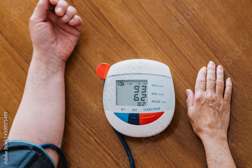 Crop anonymous elderly lady using digital sphygmomanometer while checking blood pressure photo