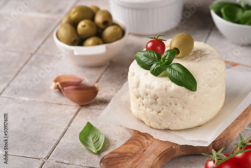 Ricotta cheese. Homemade Ricotta cheese with basil, garlic, tomatoes and green olives on parchment paperback and stand on old beige tiles background. Italian food.  Selective focus.