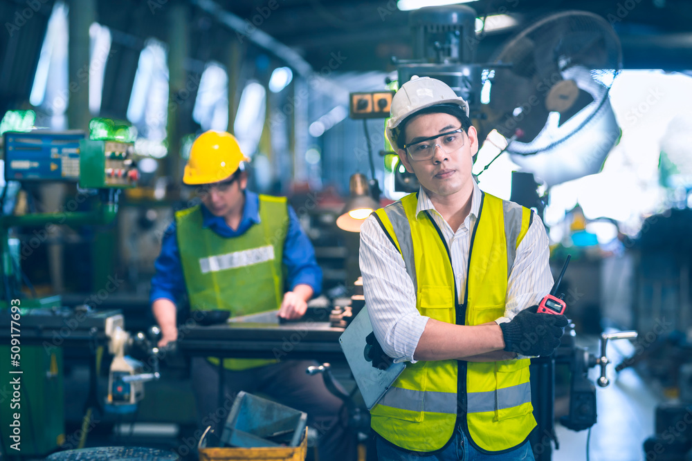 Fototapeta premium The engineer white cross one's arm hole the tablet and walkie talkie front of the working yellow safety helmet working with machinery in industrial