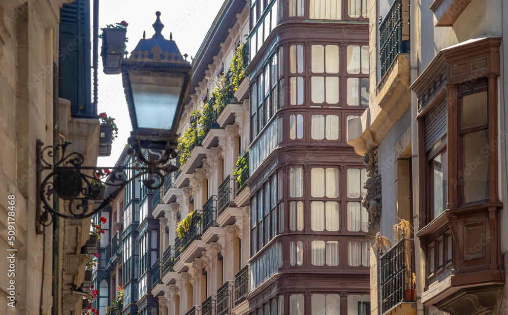 Fasada zabytkowego  budynku , w tle ulica , na pierwszym planie latarnia. Bilbao