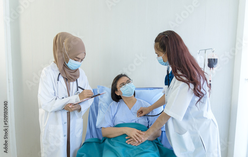 Photography Muslim female doctor giving advice discussion and young Asian female doctor using stethoscope checking pressure to elderly patient sitting in bed at hospital