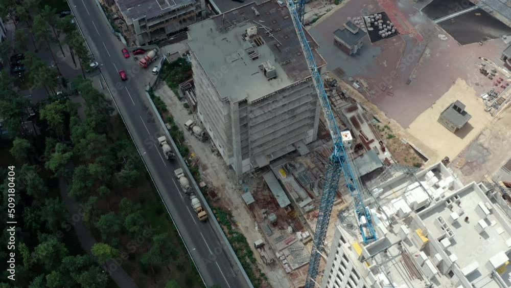 Construction of new apartments in the city near the park. Reconstruction and restoration of the city. Construction of multi-storey houses: construction site with crane and builders: drone shot. Construction of new apartments in the city near the park. Reconstruction and restoration of the city. Construction of multi-storey houses: construction site with crane and builders: drone shot.
