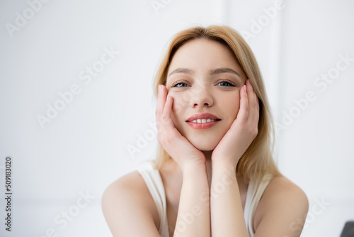 Pretty young woman touching face and looking at camera at home.
