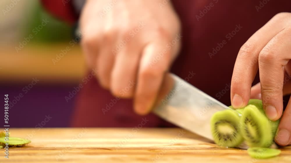Male's hand cutting fresh kiwi on cutting board. Cook in uniform slicing fresh fruit with professional knife. Making smoothies. Cutting fruits for cocktail. Cutting fresh kiwi for for healthy fruit Male's hand cutting fresh kiwi on cutting board. Cook in uniform slicing fresh fruit with professional knife. Making smoothies. Cutting fruits for cocktail. Cutting fresh kiwi for for healthy fruit