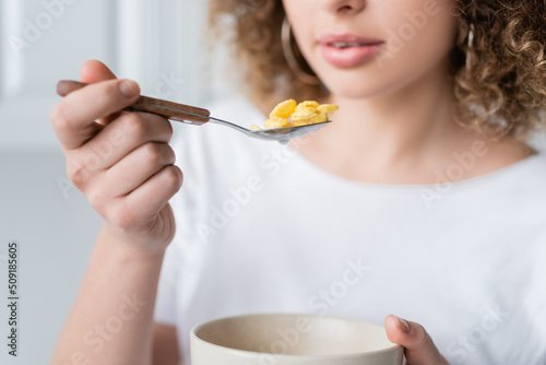 partial view of blurred woman with bowl and spoon of delicious corn flakes.