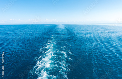 Footprint on the water from the ship. White wave on blue water. Blue sea water. Water and sky.