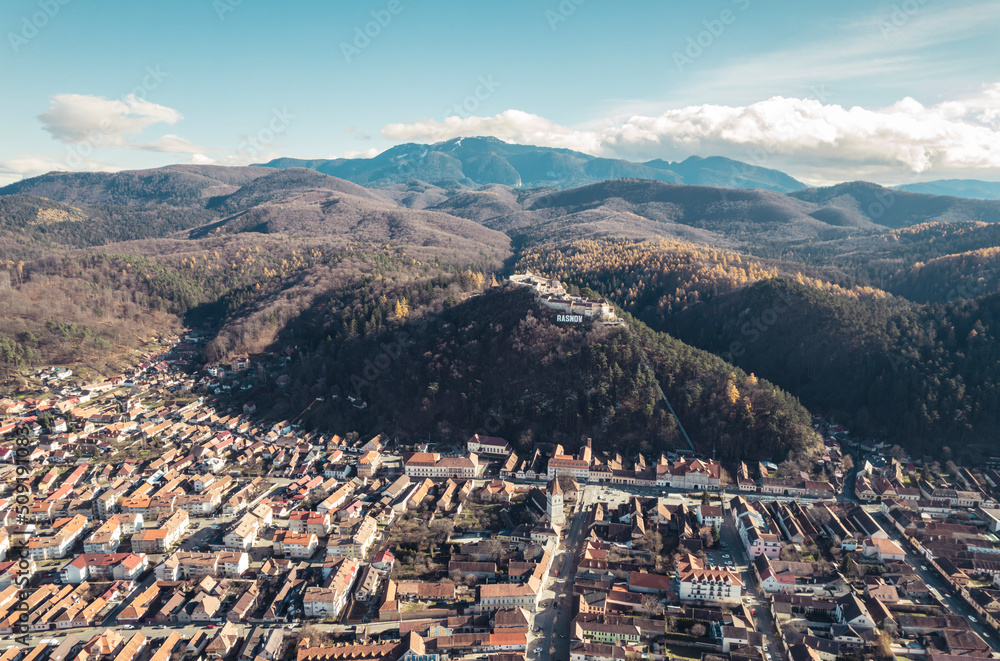Obraz premium Aerial view of Rasnov, Romania shows that the buildings are styled with medieval fortress architecture. Medieval fortification in Brasov. Drone shot of Rasnov Medieval city