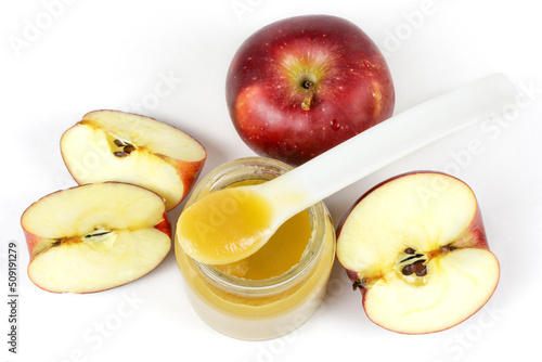 Baby food. A glass jar with baby apple puree with a spoon and red ripe apples on a white isolated background. The first fruit lure of the baby.