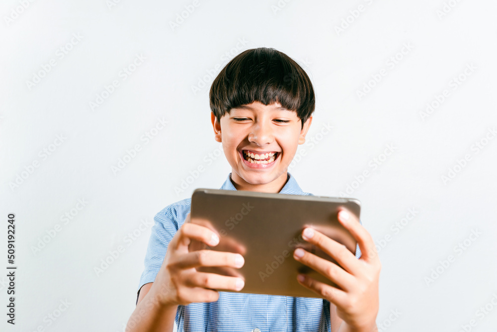 Preteen mix race boy kid in school uniform using a tablet computer mobile to online e-learning, social media for texting chatting or play a game on white background. Child technology study concept Preteen mix race boy kid in school uniform using a tablet computer mobile to online e-learning, social media for texting chatting or play a game on white background. Child technology study concept