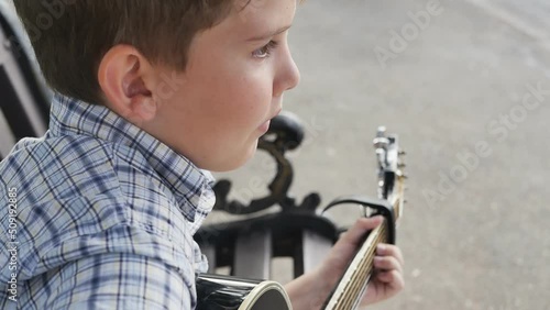 Wallpaper Mural cute european teenager playing acoustic guitar sitting on a street bench close to the road and pavement. The boy earns money by playing a melody. slow motion Torontodigital.ca