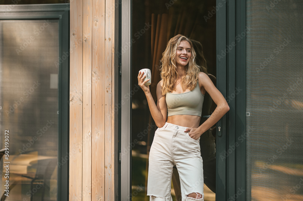 Joyful blonde woman standing at the house entrance