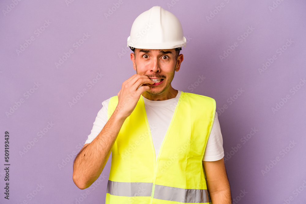Young hispanic worker man isolated on purple background biting fingernails, nervous and very anxious.