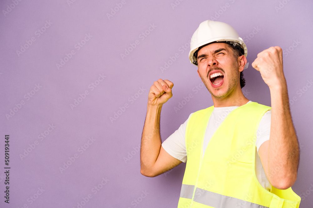 Young hispanic worker man isolated on purple background raising fist after a victory, winner concept.