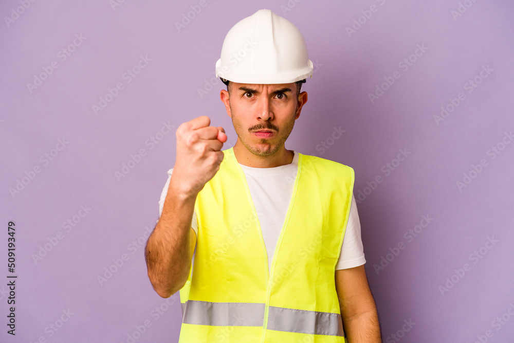 Young hispanic worker man isolated on purple background showing fist to camera, aggressive facial expression.