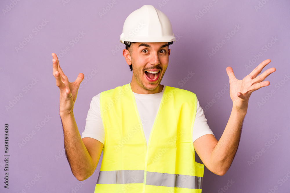 Young hispanic worker man isolated on purple background receiving a pleasant surprise, excited and raising hands.