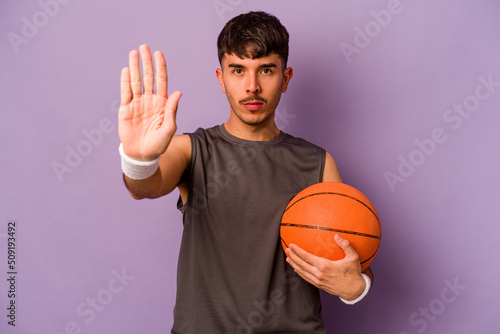 Young hispanic basketball player man isolated on purple background standing with outstretched hand showing stop sign, preventing you. © Asier