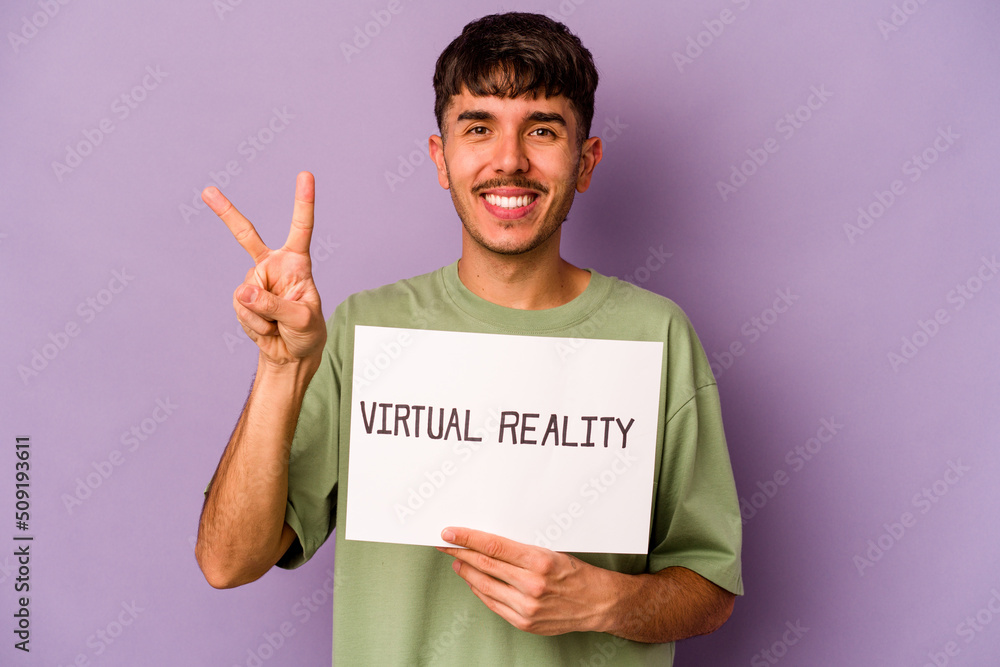 Young hispanic man holding virtual reality placard isolated on purple background showing number two with fingers. Young hispanic man holding virtual reality placard isolated on purple background showing number two with fingers.