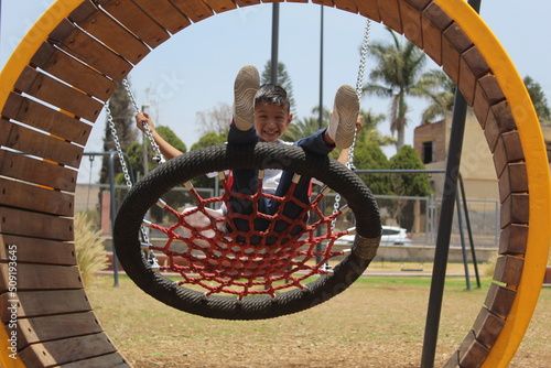 Niño jugando en un columpio de rueda tejida con una red roja en un día soleado