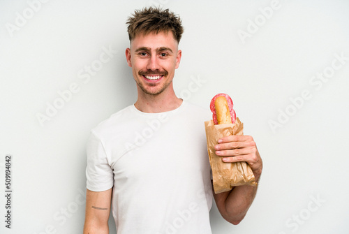 Quadro em tela Young caucasian man holding a sandwich isolated on white background happy, smiling and cheerful