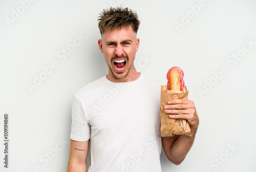 Young caucasian man holding a sandwich isolated on white background screaming very angry and aggressive.