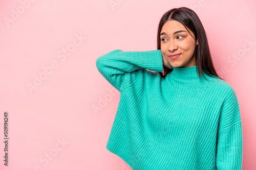 Young hispanic woman isolated on pink background touching back of head, thinking and making a choice. © Asier