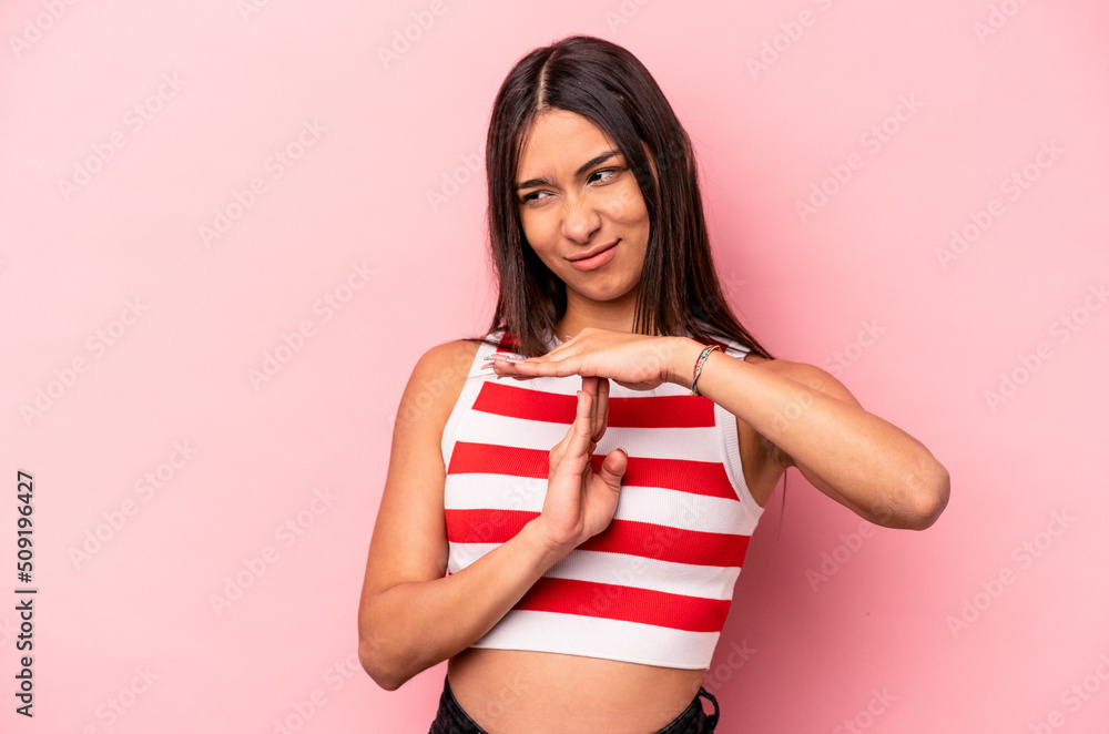 Young hispanic woman isolated on pink background showing a timeout gesture.
