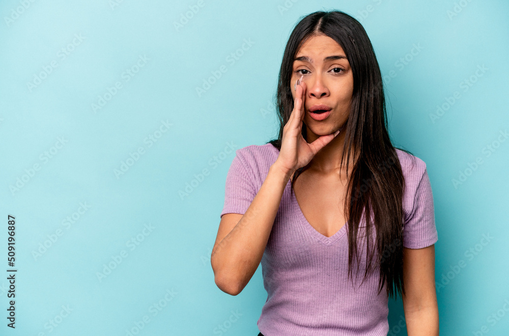 Young hispanic woman isolated on blue background is saying a secret hot braking news and looking aside Young hispanic woman isolated on blue background is saying a secret hot braking news and looking aside