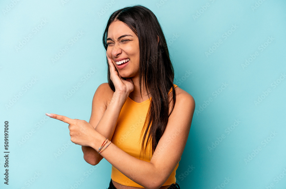 Young hispanic woman isolated on blue background saying a gossip, pointing to side reporting something. Young hispanic woman isolated on blue background saying a gossip, pointing to side reporting something.