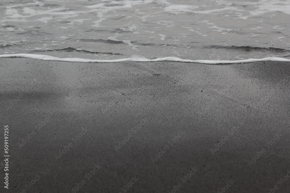 Wet black volcanic sand with sea wave with foam as line on seashore, texture, background. Wet black volcanic sand with sea wave with foam as line on seashore, texture, background.